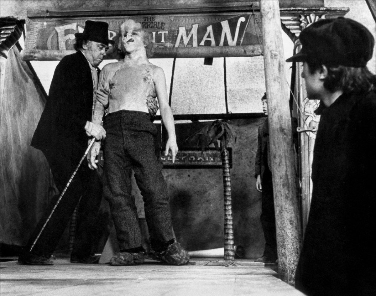 Ringmaster Mr. Bytes (Freddie Jones) exploits The Elephant Man (John Hurt) at a Victorian freak show.